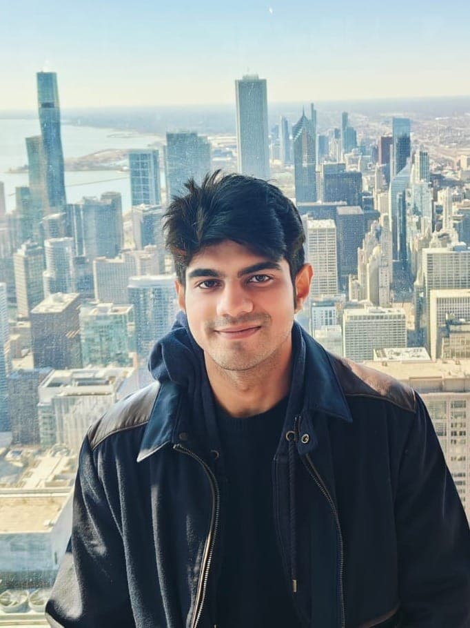 Rishabh in a dark jacket high above the Chicago skyline, downtown towers and Lake Michigan behind him.
